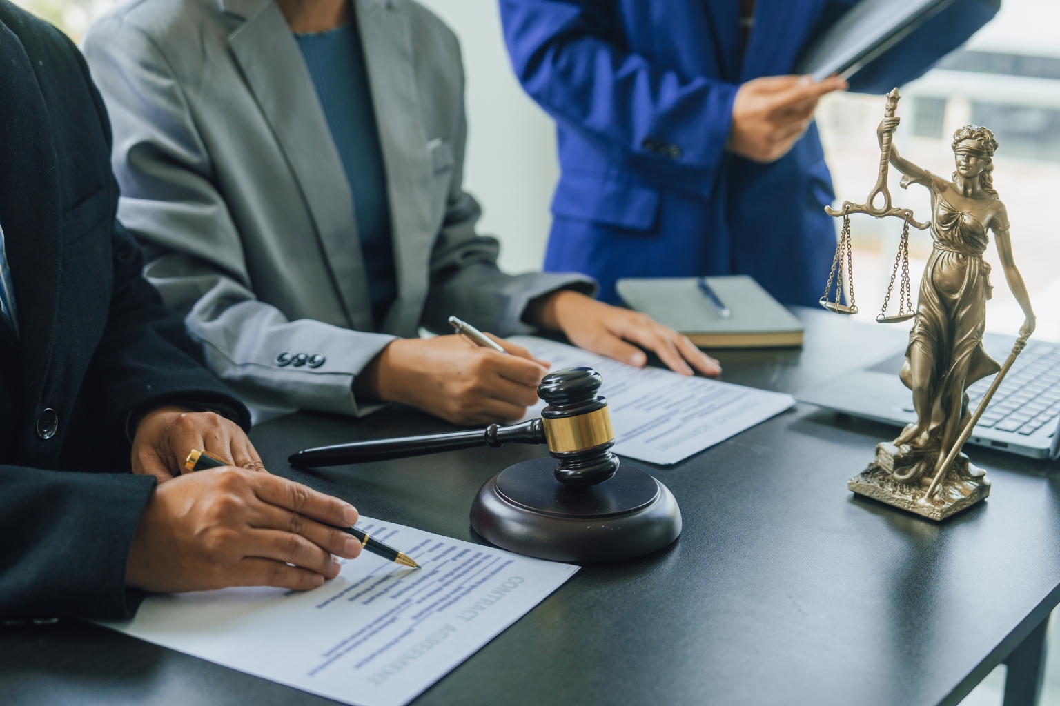 Avocats signant un contrat de cession de droit avec marteau de justice et statue de la Thémis sur le bureau
