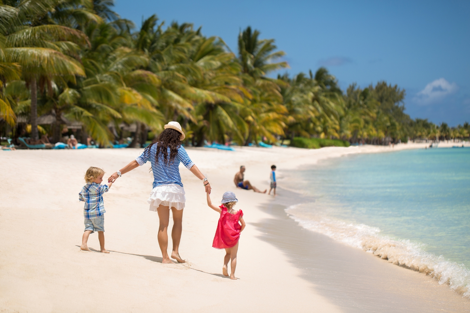 Mère et ses deux enfants se promenant main dans la main sur une plage tropicale pendant leurs congés annuels